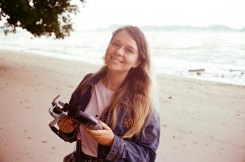 lady with a drone and its remote on hand smiling at the camera.